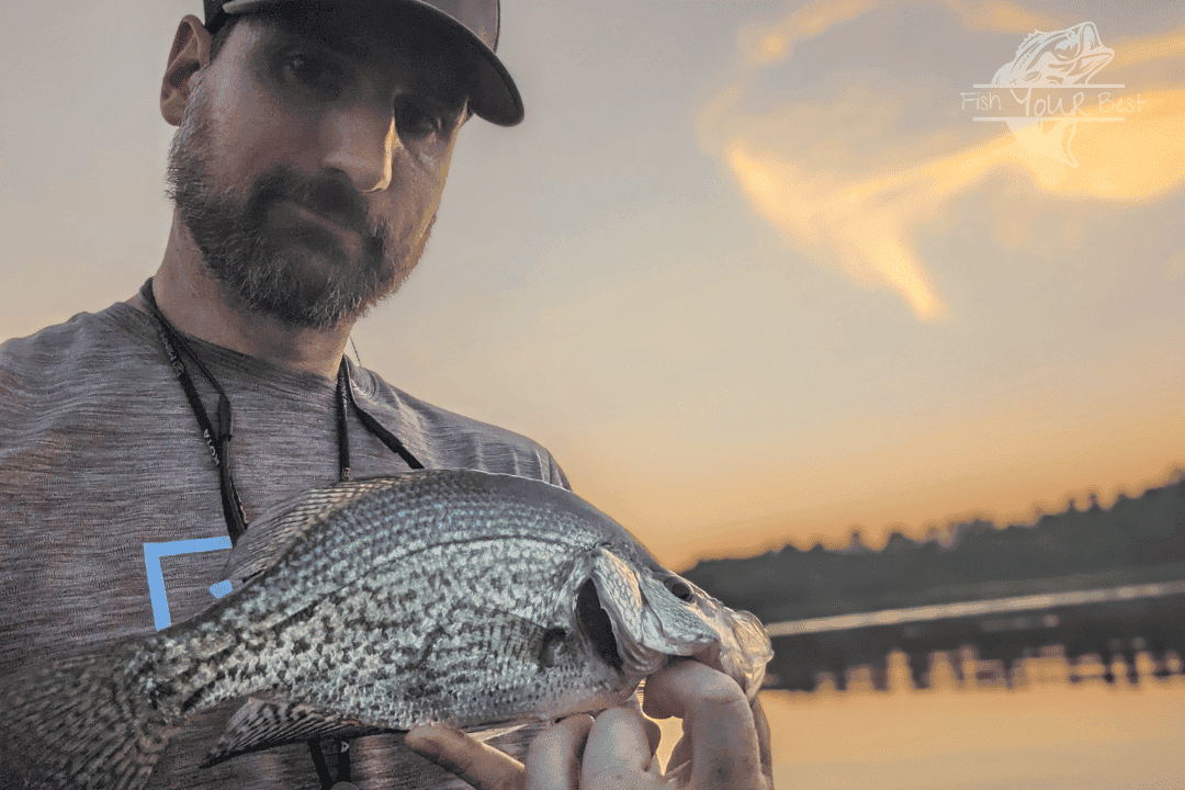 Angler holding fish with lake and sky in the background.