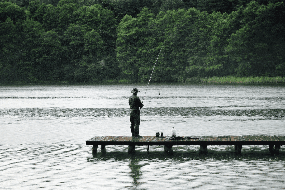 Man jig fishing in rain from dock.