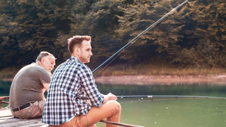 Two anglers sit on a dock with their lines cast fishing for crappie.