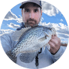 Image of the angler holding a crappie with water in the background.